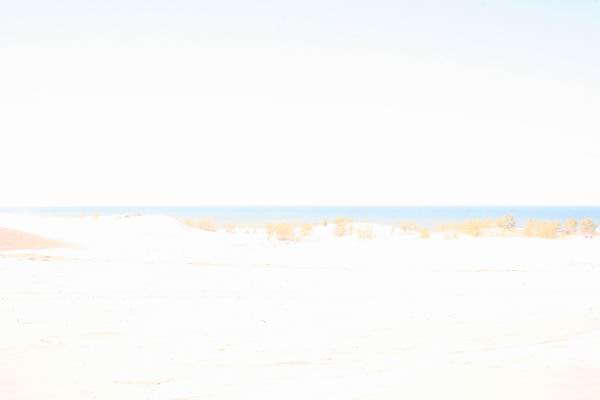 Sandy dunes and blue ocean under a bright sky with a "SUPERMOTORS www.supermotors.net" watermark