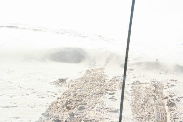 Tire tracks in sand dunes with a vertical pole on the right