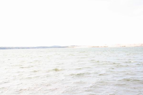 Water with waves and a distant tree line under a bright sky