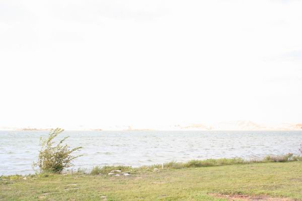 Water and grassy shore with a small bush under a bright sky, "SUPERMOTORS" logo in the corner