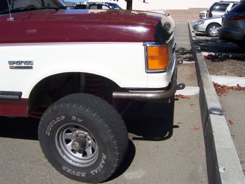 1991 Ford Bronco - Maroon and white Ford Bronco with a custom tubular front bumper, seen from the front three-quarter angle.