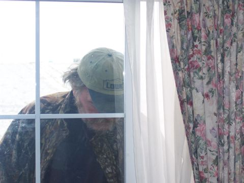 1972 Ford Ranchero - Man in camouflage jacket and Lowe's cap looks through a window with floral curtains.
