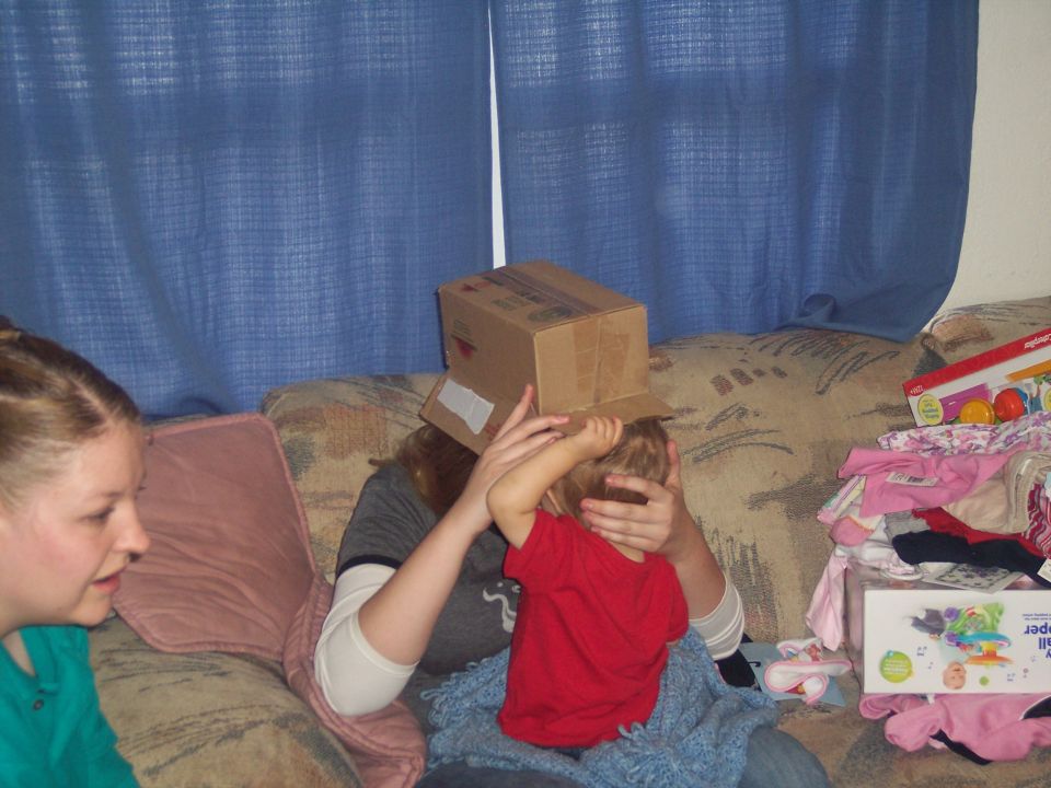 Kid wearing a cardboard box on head while sitting on a couch with a woman