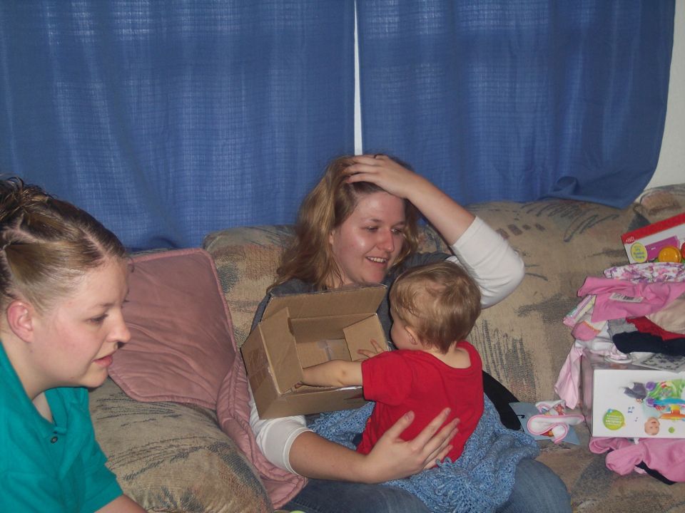 Woman holding a baby on a couch with another woman to the left and gifts to the right