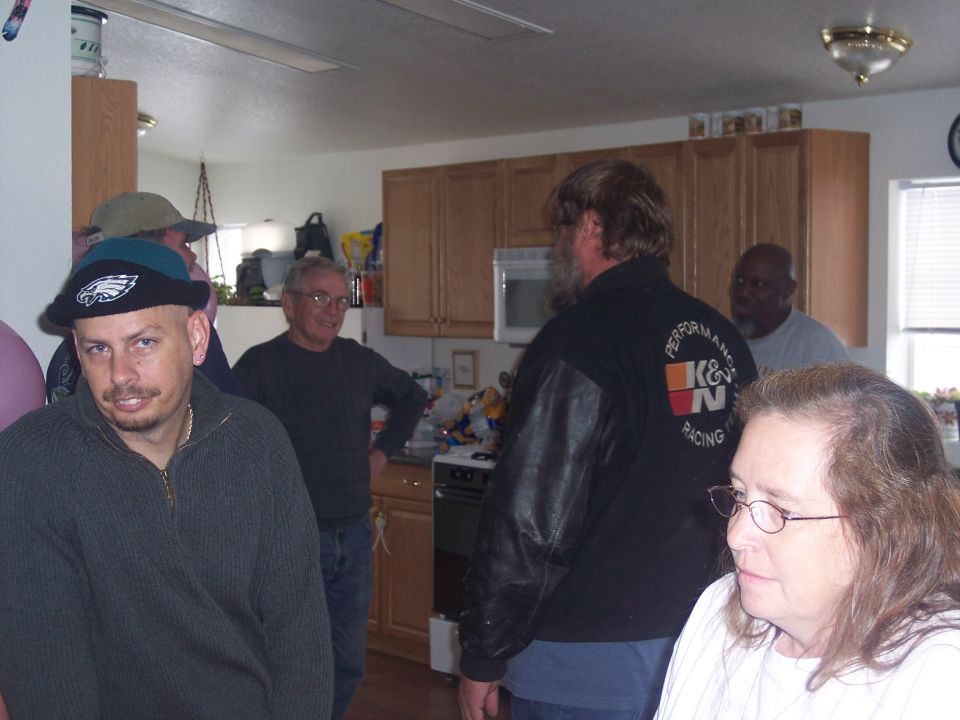 Four people gathered in a kitchen, one wearing a K&N Racing jacket