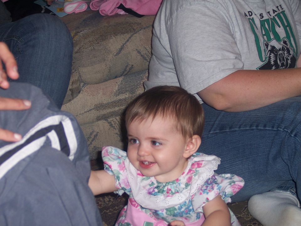 Baby in floral dress sitting on a couch with people