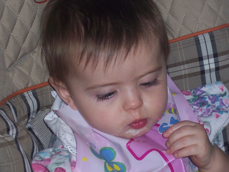 Baby wearing a pink bib with butterflies, looking down with food around its mouth