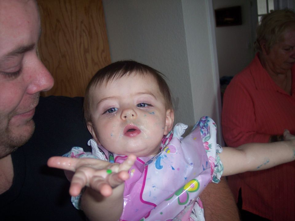 Baby with blue and green paint smudges on face and hands, wearing a pink bib