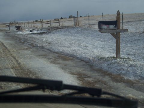 1972 Ford Ranchero - View from inside a vehicle driving on a snowy and icy rural road, passing a wooden fence and mailbox.