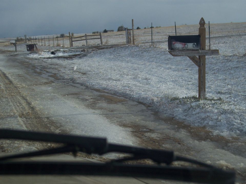 Windshield wipers on a snowy, icy road with a mailbox and fence