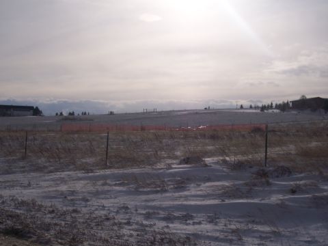 1972 Ford Ranchero - A wide view of a snowy field with a red fence in the mid-ground and distant buildings under a bright, hazy sky.