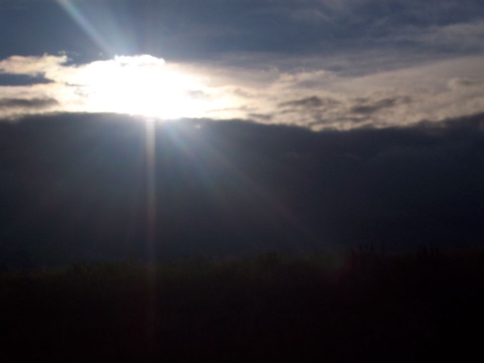 Dark clouds obscure the sun, casting rays of light downwards over a dark, indistinct landscape