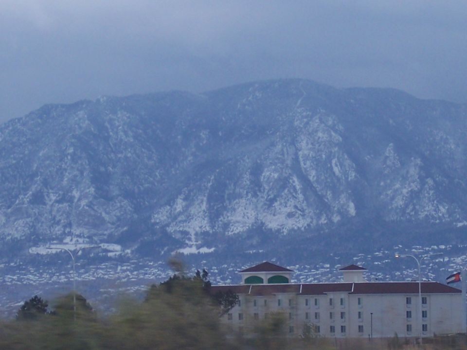 Snow-covered mountains loom over a white building with a red roof