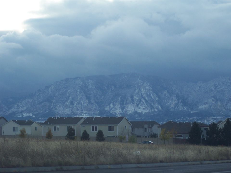 Snow-capped mountains loom over a row of suburban houses and dry grass