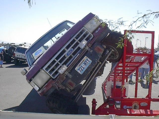 Maroon Ford 4x4 pickup tilted nose-up on a red ramp outdoors