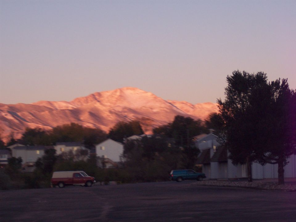 Red pickup truck with a white camper shell and a teal SUV parked in a lot with a mountain in the background
