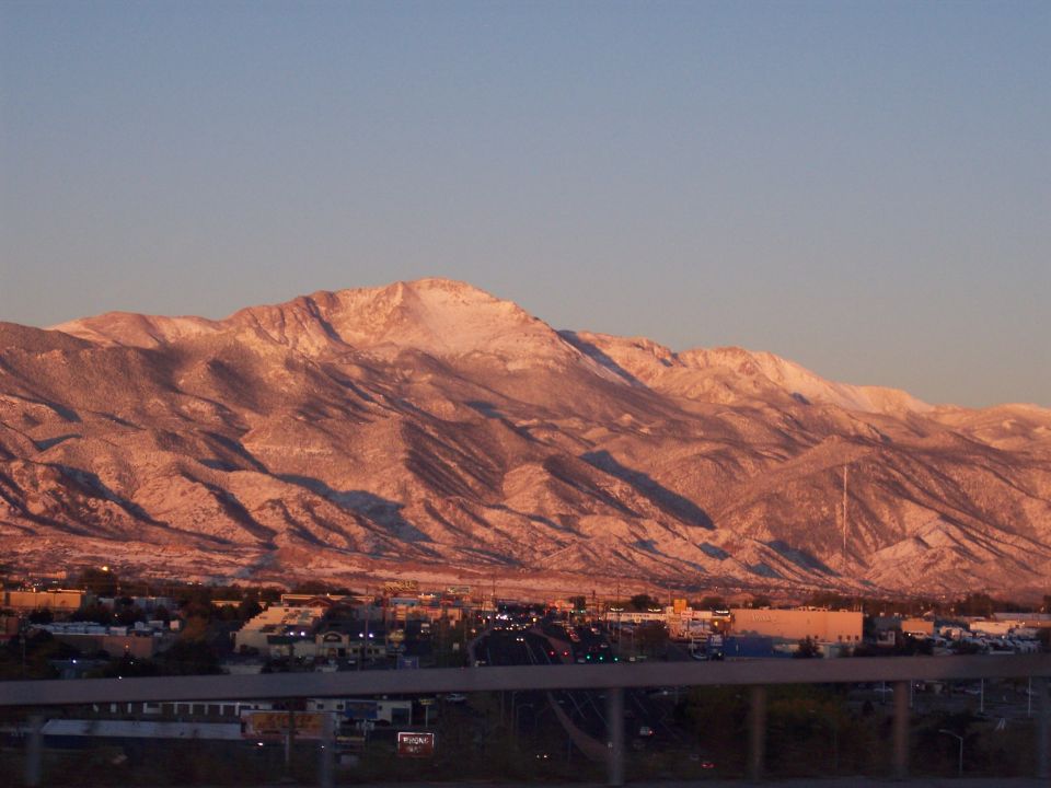 Snow-capped mountains glow pink at sunset over a city skyline