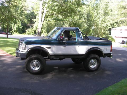 1994 Ford Bronco - Side view of a lifted green and white Ford Bronco parked on asphalt.
