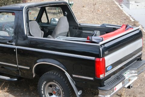 1994 Ford Bronco - Rear three-quarter view of a black full-size Ford Bronco with the hardtop off, showing roll bar padding and tailgate.