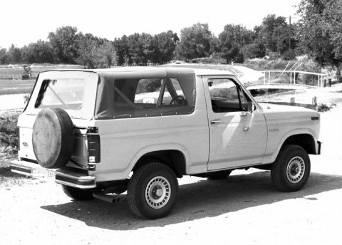 1994 Ford Bronco - Black-and-white 3/4 rear passenger-side photo of a full-size Ford Bronco fitted with a light-colored soft top with zip-out side and rear wi…