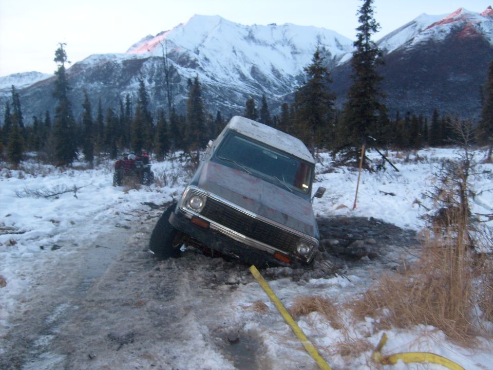 Brown Chevrolet K5 Blazer stuck in snow, front wheel deep in mud, with an ATV in the background