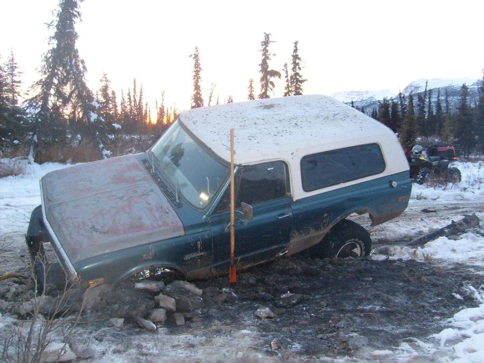 Green and white 1979 Chevrolet Blazer stuck in mud and snow, with an ATV in the background