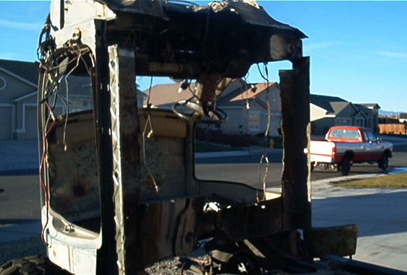 Demolished vehicle chassis in foreground, red and silver pickup truck in background