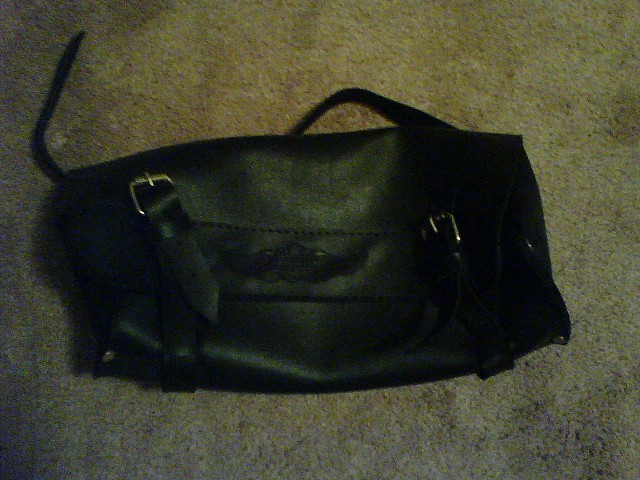 Black leather motorcycle saddlebag with buckles on a carpeted surface
