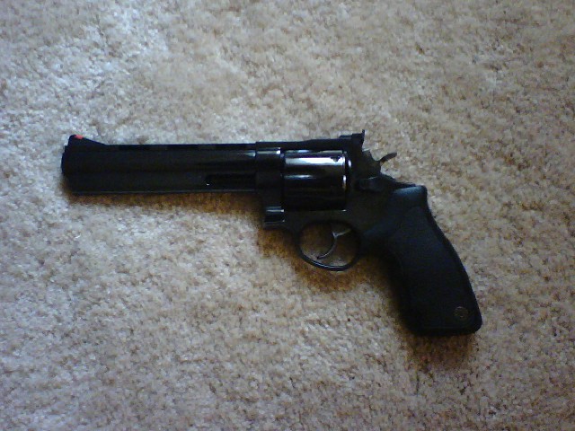 Blued long-barrel revolver with black rubber grips lying on beige carpet