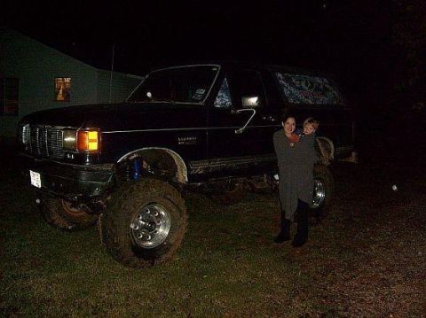 1989 Ford Bronco - A lifted Ford Bronco is parked on grass at night with two people standing next to it.