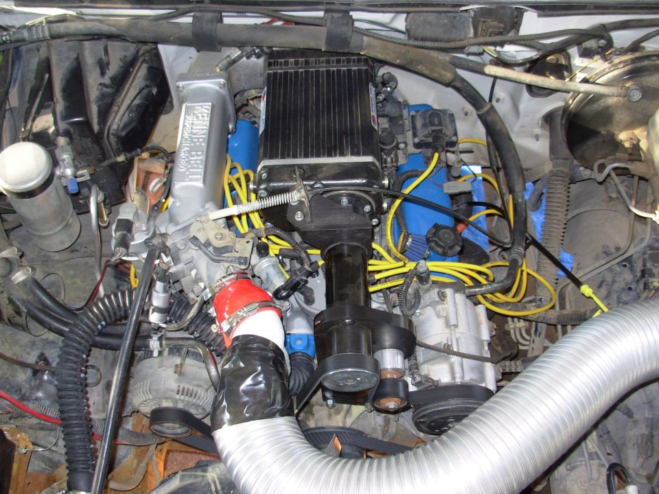 Engine bay showing a large silver intake manifold with text, yellow spark plug wires, and various hoses and components