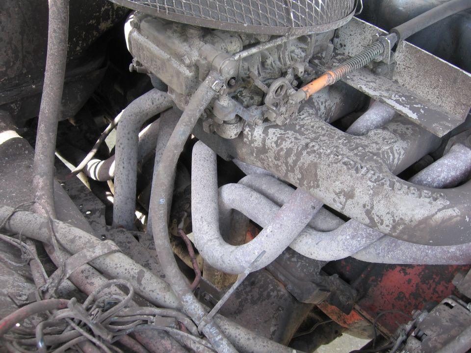 close-up of a dirty engine bay showing exhaust pipes and carburetor