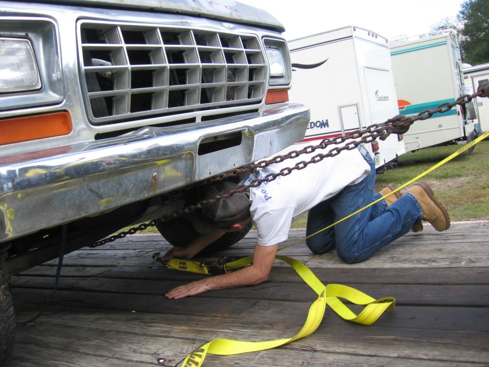 Man securing a 1979 Ford F-150 to a trailer with chains and straps. RVs are in the background