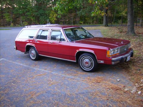 1982 Ford LTD Crown Victoria - Red station wagon parked in a lot with trees in the background. The vehicle is a full-size, rear-wheel-drive wagon.