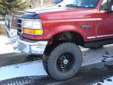 1996 Ford Bronco - 1996 Ford Bronco in red, showing the front quarter panel and wheel with snow on the ground.