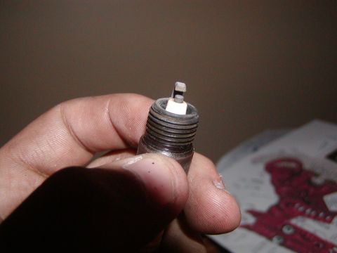 1991 Ford Bronco - A close-up view of a used spark plug, held by a person's fingers.