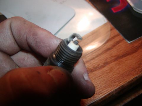 1991 Ford Bronco - A spark plug is shown being held by a hand, with a wooden surface in the background.