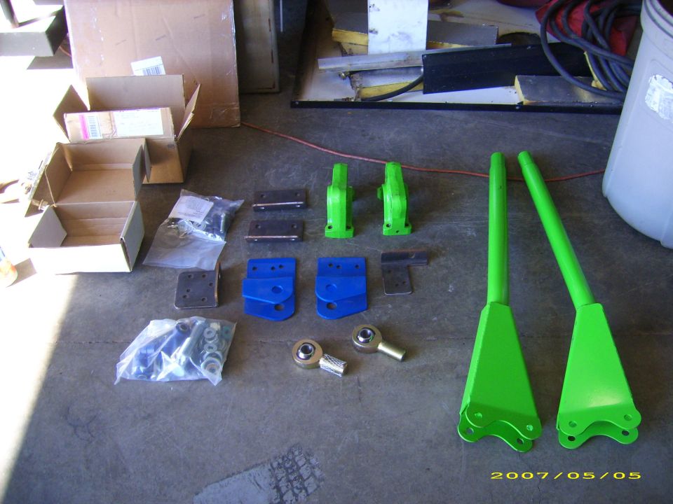 Green and blue suspension link kit parts laid out on a garage floor