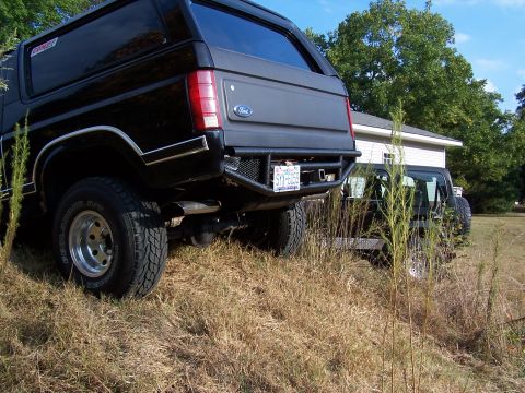 1983 Ford Bronco - Black Ford Bronco and another SUV parked on grassy terrain.