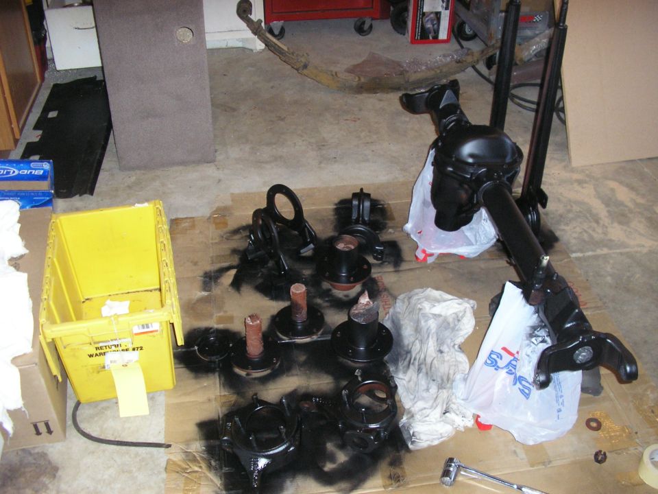 Various black automotive parts, including a differential and hubs, laid out on cardboard on a garage floor