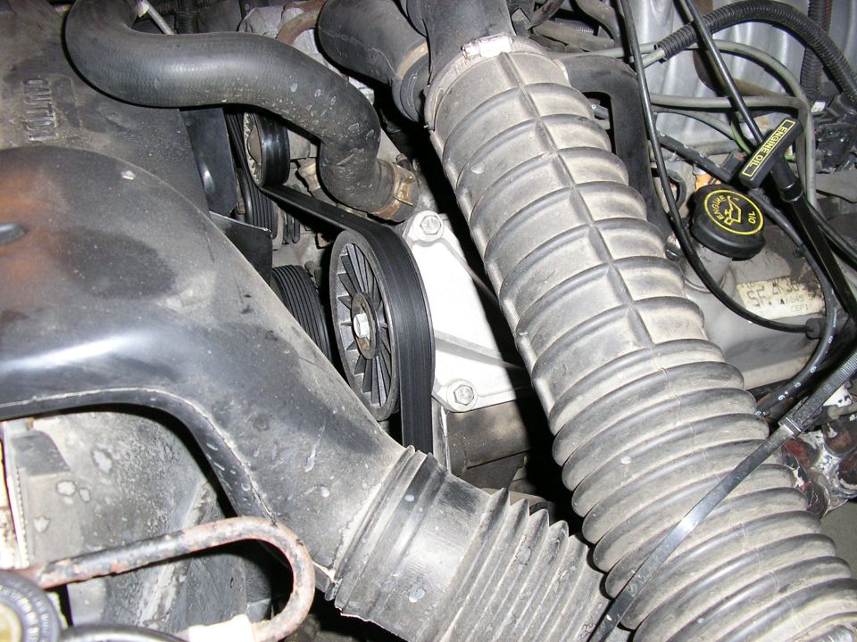 Close-up of engine bay showing ribbed air intake hose, belts, and pulleys