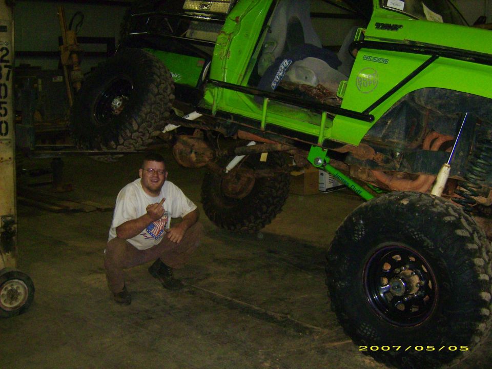 Man kneeling beside a green lifted truck flexed on a large tire
