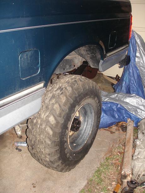 1996 Ford F-150 - The rear wheel well of a truck is shown, with a large tire and a blue tarp in the background.