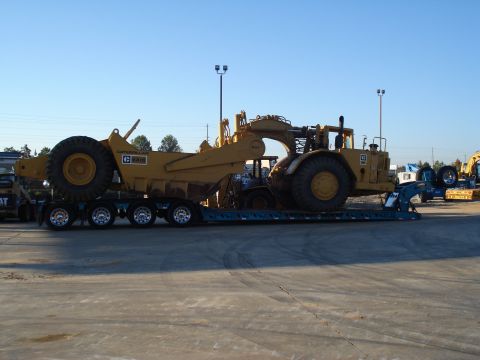 1966 International School Bus - Caterpillar scraper being transported on a flatbed trailer under a clear blue sky.