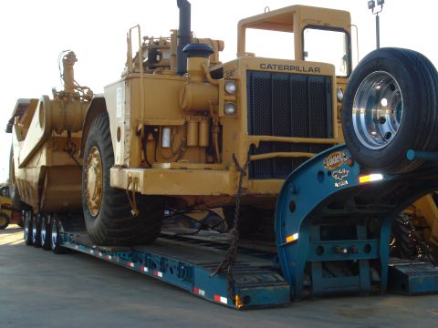 1966 International School Bus - A large yellow Caterpillar mining truck is transported on a flatbed trailer.