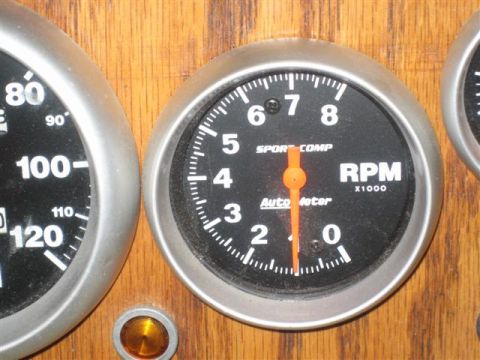 1900 Yugo Vega - Close-up of dashboard gauges, including a tachometer and speedometer, set against a wooden background.