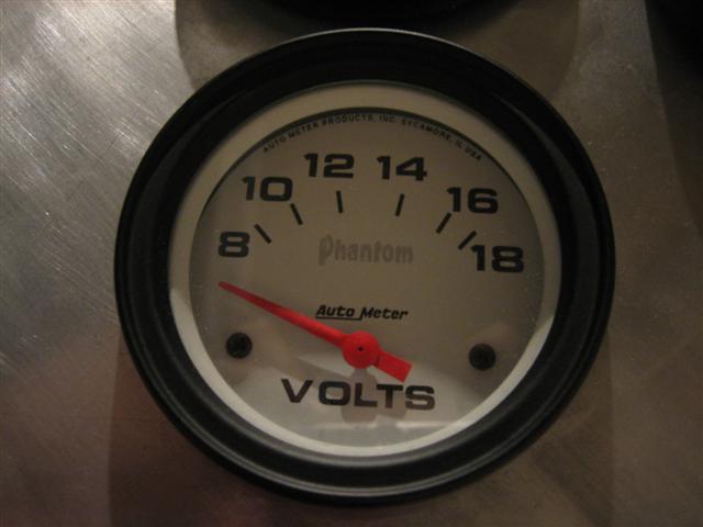 Close-up of a Phantom Auto Meter voltmeter gauge with a red needle pointing to about 10