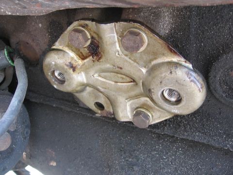 1979 Ford F-150 - Close-up of a stamped-steel engine mount bracket bolted to the side of a black engine block, its two threaded bosses empty and the surround…