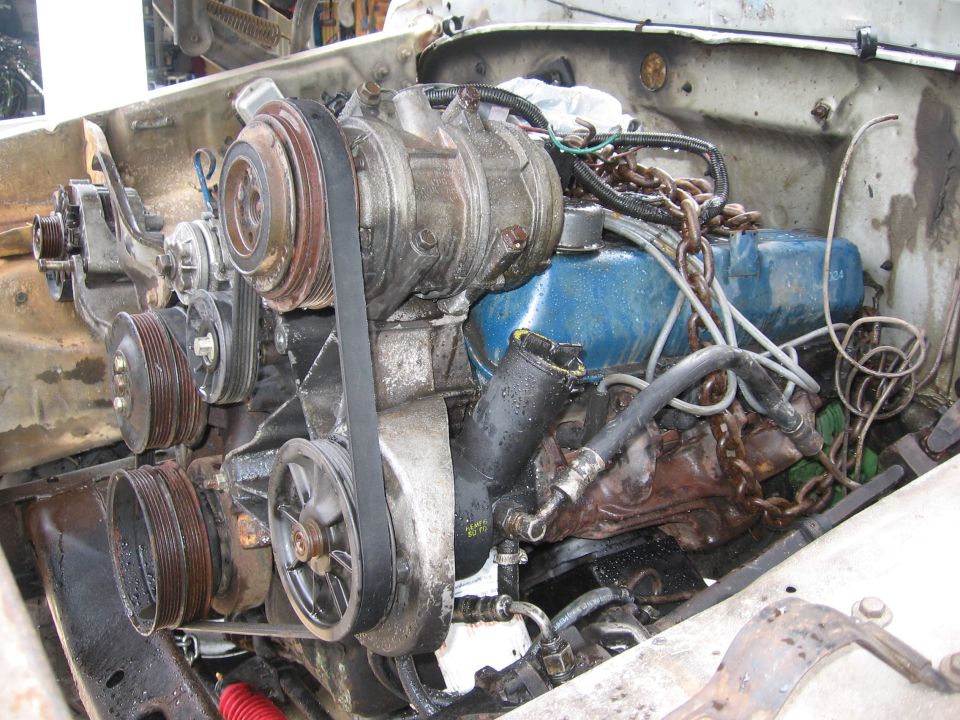 Engine bay showing V-belt system, air conditioning compressor, and blue valve covers