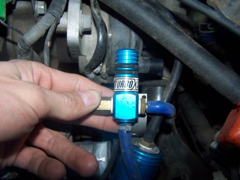 1994 Ford Probe - A hand holds a blue turbo valve labeled 'TURBOX', part of an engine bay.